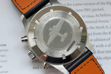 Close-up of luxury pilot watch stainless steel caseback with engraved airplane and orange leather strap