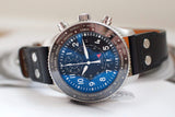 Luxury chronograph watch with blue dial, time zone bezel, and black leather strap