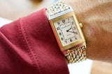 Close-up of a Jaeger-LeCoultre Reverso luxury watch with a gold and steel bracelet on a wrist.