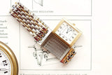 Vintage gold and silver luxury wristwatch with a square face on a technical drawing background