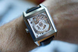 Square Swiss luxury skeleton watch with visible movement on wrist, black leather strap
