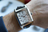 Square silver luxury GMT watch with white dial and black leather strap on wrist