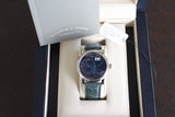 Luxury silver watch with black dial and date display in box, green leather strap