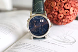 Luxury stainless steel watch with black dial and green leather strap on an open book