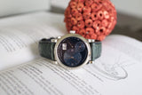 Luxury black dial watch with green alligator strap resting on open book, elegant style