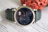 Close-up of a luxury wristwatch with dark dial, large date display, and green leather strap