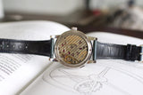 Luxury mechanical watch with visible movement and black leather strap displayed on an open book