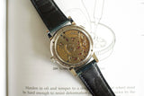 Luxury watch with visible gold mechanical movement and black leather strap on open book