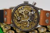 Vintage chronograph watch with exposed gold and steel movement, brown leather strap