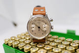 Vintage Lemania chronograph watch with brown leather strap on ammunition case