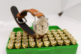 Vintage Lemania chronograph watch with brown leather strap displayed on a box of brass ammunition