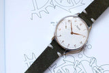 Silver dial Minerva limited edition men's watch with green leather strap on open book
