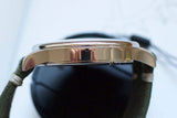 Close-up side view of a luxury men's watch with a polished metal case and green strap