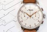 Vintage Minerva chronograph watch with a white dial and brown leather strap over blueprints.