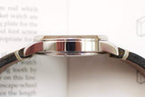 Side profile of a luxury Swiss watch with a polished silver case and brown leather strap.
