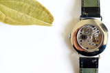 Back view of a luxury mechanical wristwatch with visible movement and green leather strap