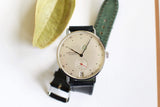 Minimalist Nomos mechanical wristwatch with black leather strap on white background