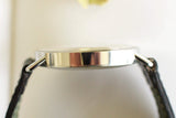 Side view of a slim silver luxury watch case with black leather strap