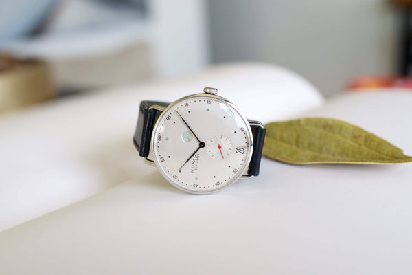 Minimalist luxury watch with white dial, black leather strap, and small seconds subdial