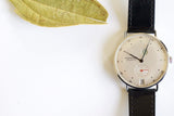 Minimalist luxury watch with black leather strap and white dial on white background