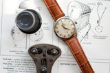 Vintage Omega Constellation gold watch with brown leather strap on technical blueprints