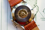 Case back of a luxury Swiss watch with a planetary emblem and brown leather strap