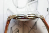 Close-up side view of a luxury watch case and Omega logo on the crown with a brown leather strap.
