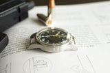 Vintage military-style luxury watch with black dial and silver case on technical paper