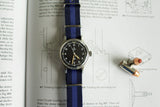 Omega Fat Arrow military watch with blue NATO strap on technical book, next to two bullets