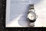 Omega Seamaster GMT luxury watch with stainless steel bracelet resting on a book page.