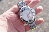 Hand holding a pre-owned Omega Seamaster GMT luxury watch with a silver dial and steel bracelet
