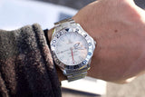 Close-up of an Omega Seamaster GMT watch with a silver dial and steel bracelet on a wrist.