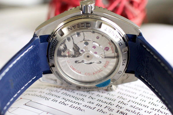 Close-up of Omega Seamaster Liquidmetal watch back, blue strap, visible movement, luxury timepiece.