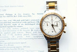 Omega Speedmaster luxury watch with a gold and steel bracelet resting on a document.