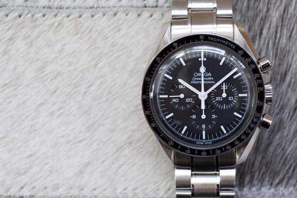 Stainless steel Omega Speedmaster Professional chronograph watch with black dial on textured surface