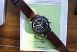 Omega Speedmaster chronograph watch with a brown leather strap on a technical document