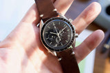 Close-up of an Omega Speedmaster Professional luxury watch with a brown leather strap.