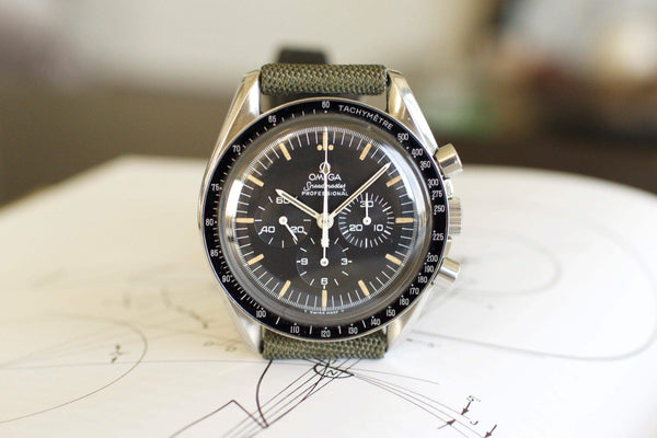 Vintage Omega Speedmaster chronograph watch with black dial and tachymeter bezel on green strap