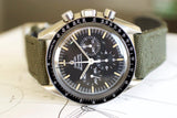 Vintage Omega Speedmaster chronograph with black dial, tachymeter bezel, and green fabric strap