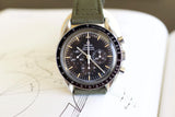 Omega Speedmaster Professional watch with black dial, tachymeter bezel, and green fabric strap