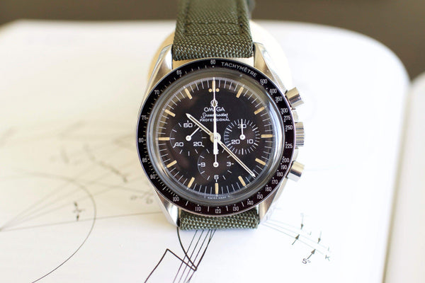 Omega Speedmaster Professional watch with black dial, tachymeter bezel, and green fabric strap