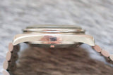 Side view of a stainless steel watch case and bracelet on a textured surface