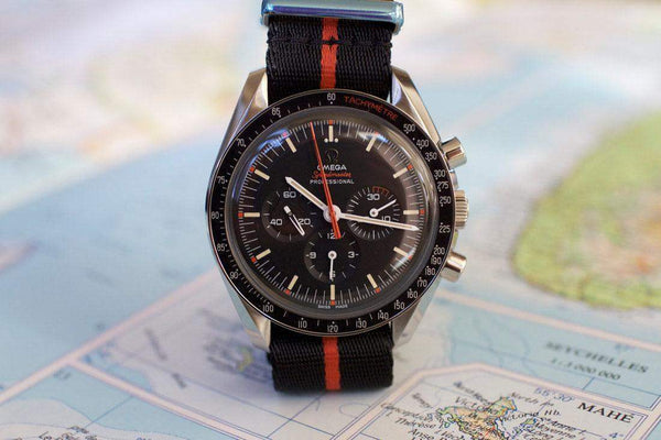Omega Speedmaster black chronograph watch with orange stripe NATO strap on a map
