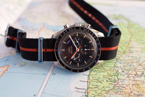 Omega Speedmaster black chronograph watch with orange NATO strap on a map background
