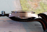 Side view of a luxury stainless steel watch case with a black strap on a map