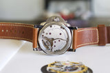 Close-up of Panerai watch caseback with brown leather strap and visible mechanical movement.