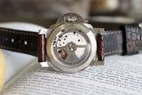 Close-up of a luxury Swiss watch with open caseback and brown leather strap on a book