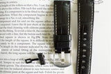 Black leather watch strap with white stitching and metal buckle on open book