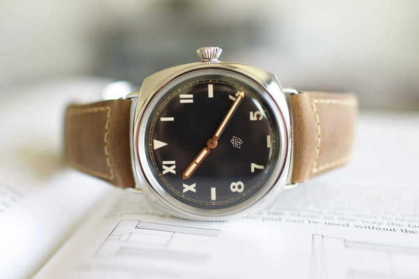 Luxury Swiss watch with black dial, tan leather strap, and gold hands on open book