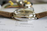 Luxury Swiss watch with brown leather strap, close-up side view on technical documents